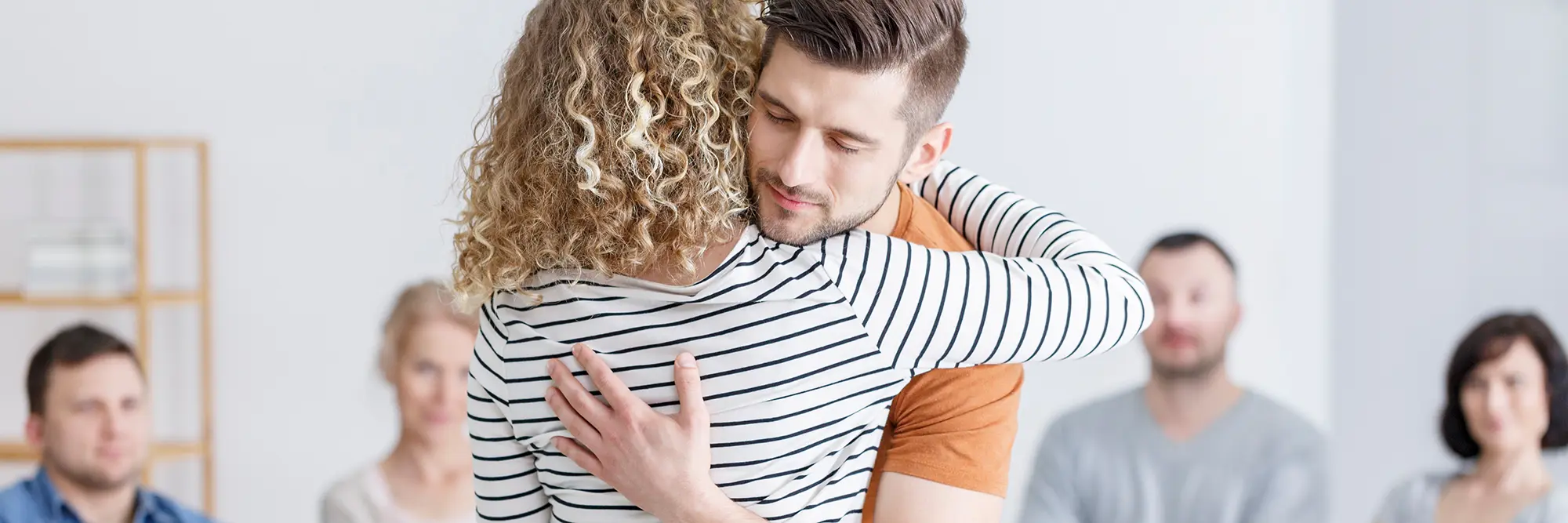 2 individuals hugging each other while attending an AA meeting