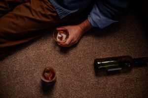 Man lying on floor with glass of alcoholic beverage and empty bottles nearby
