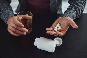 Man holding glass of alcoholic beverage with handful of pills representing Seroquel