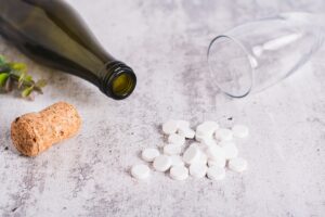 Empty alcohol bottle and overturned glass next to pills representing Wellbutrin