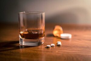Glass of alcohol next to pills representing Zoloft on table near open medication container
