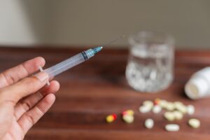Injector pen for Ozempic or other similar GLP-1 medication next to glass of clear alcohol and pills on table