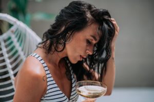 Woman holding head and looking tired with glass of alcoholic beverage in hand