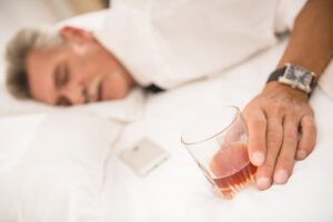 Man falling unconscious while holding half-finished glass of alcoholic drink