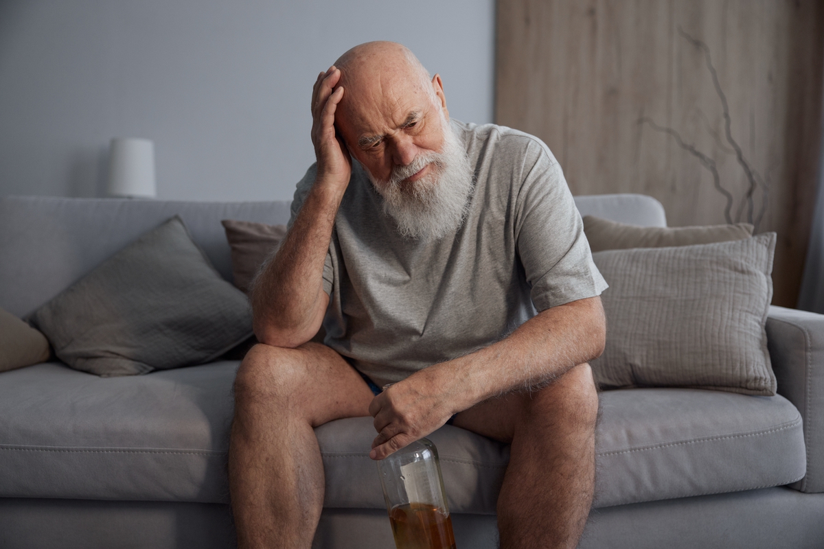 Man with confused expression and empty bottle sitting on couch to represent Wernicke-Korsakoff Syndrome